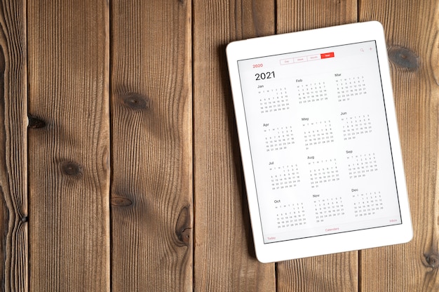 Une tablette avec un calendrier ouvert pour 2021 ans sur un fond de table en bois. espace pour le texte