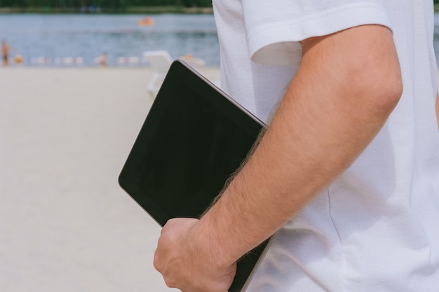 Tablette dans la main du gars sur le fond de la plage.