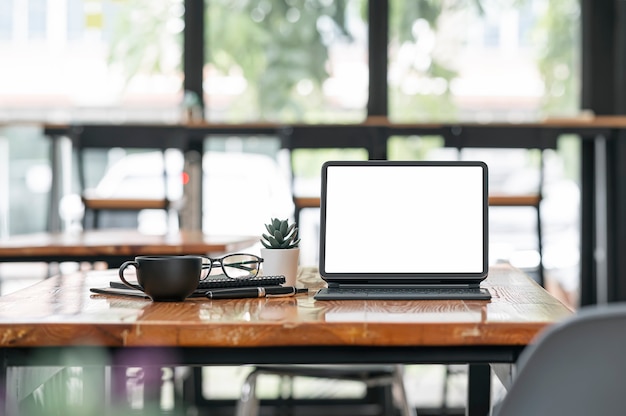 Tablette à écran blanc avec clavier magique et souples sur table en bois dans la salle du café.