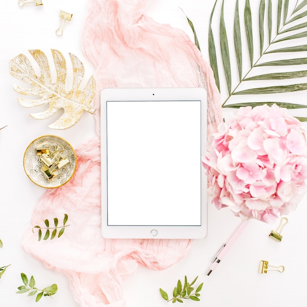 Photo tablette écran blanc, fleurs d'hortensia rose, feuille de palmier et accessoires sur surface blanche