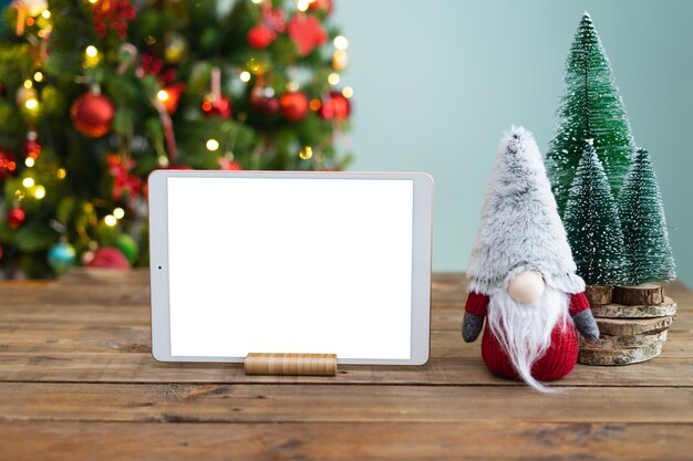 Tablette avec écran blanc sur une table avec décoration de Noël et gnome arrière-plan arbre de Noël fichier Png