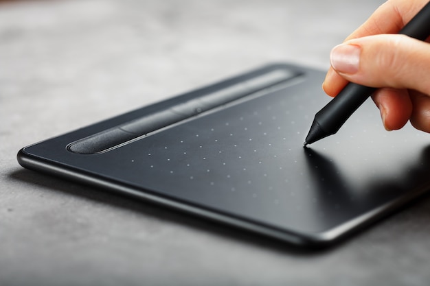 Tablette graphique avec un stylo dans les mains du designer, gros plan. Gadget pour la créativité et le travail