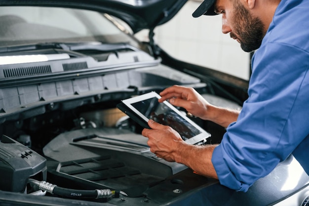 Photo avec une tablette à la main mécanicien automobile travaillant dans un garage service de réparation