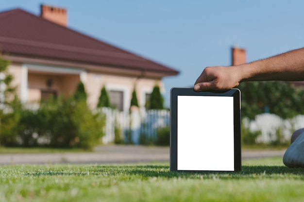 Tablette à la main, sur la pelouse sur fond de maison.