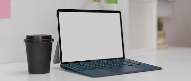 Tablette numérique avec clavier sans fil et gobelet en papier sur une table de travail moderne blanche