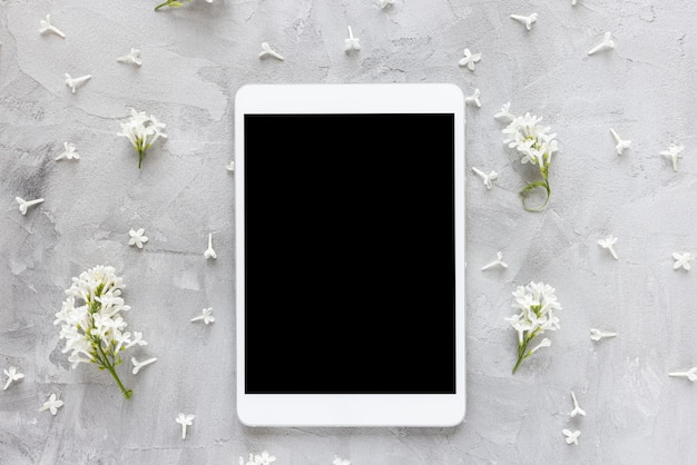 Tablette numérique sur fond floral de printemps avec des fleurs lilas blanches