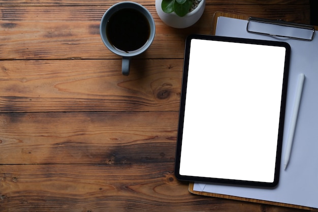 Tablette numérique vue de dessus, presse-papiers et tasse à café sur une table en bois.