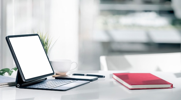 Tablette portable à écran blanc vierge avec clavier magique sur une table supérieure blanche.