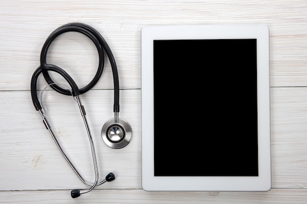 Photo tablette de table des médecins et stéthoscope bleu sur fond de bois blanc