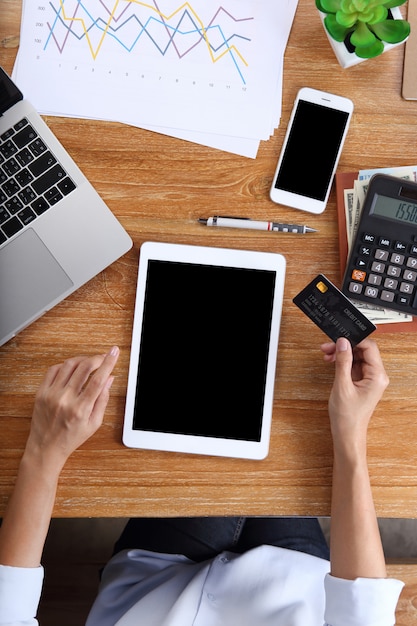 Tablette d'utilisation de femme d'affaires avec holding papeterie de carte de crédit, smartphone et bureau sur le bureau en bois