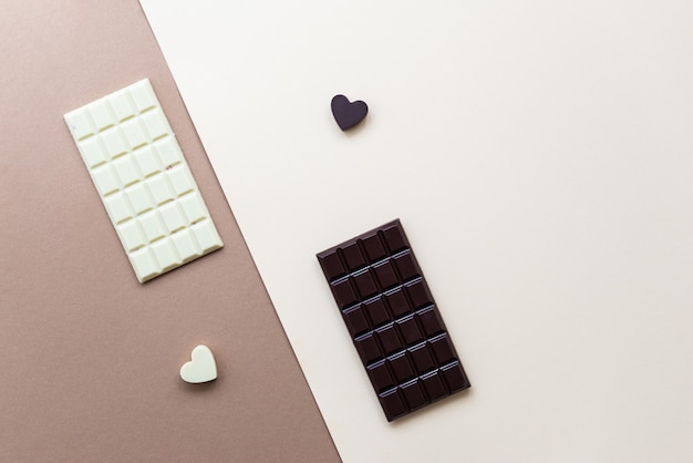 Tablettes de chocolat blanc et noir avec des coeurs sur fond marron.