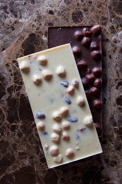 Tablettes de chocolat noir et blanc avec des noisettes entières sur une surface en marbre