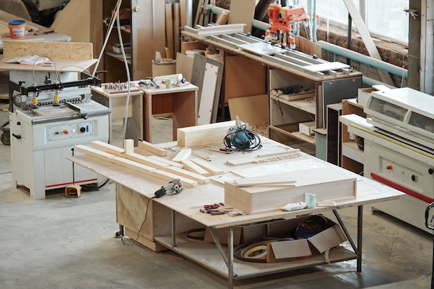 Établi d'ouvrier d'usine de meubles avec des pièces en bois, des outils à main électriques et d'autres objets entourés de divers équipements
