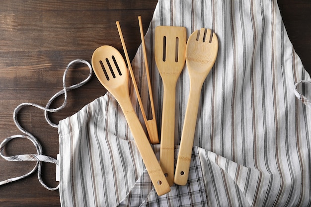 Tablier avec ustensile de cuisine sur fond de bois.