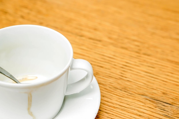 Tache de café dans une tasse blanche et une cuillère à café avec soucoupe sur une table en bois