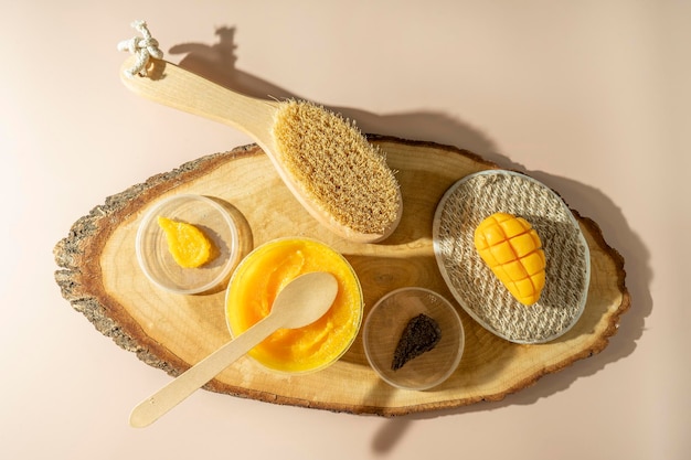 Une tache jaune d'un gommage corporel à la mangue une brosse pour le corps et un savon naturel à la mangue allongé sur un plateau en bois