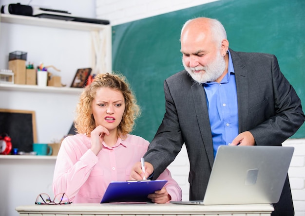 Tâches difficiles Test de connaissances Lycée université université Enseignant enseignant aidant l'étudiant à passer le test Examen de réussite Homme enseignant d'école mature et fille avec ordinateur portable Test final et remise des diplômes