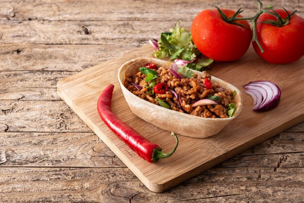 Taco barquita mexicain avec boeuf, piment, tomate, oignon et épices sur table en bois