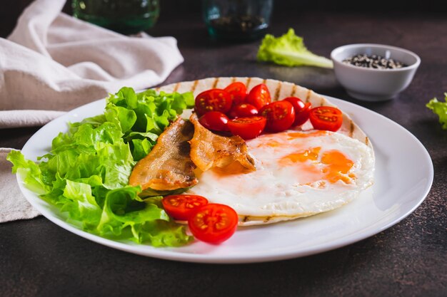 Photo des tacos appétissants avec des œufs frits, du bacon, des tomates et de la laitue sur une assiette sur la table.