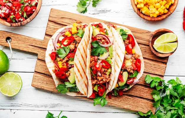 Tacos de cuisine mexicaine avec boeuf maïs haricots rouges sauce salsa tomate et oignons dans une tortilla de maïs à bord vue de dessus de fond de table blanche