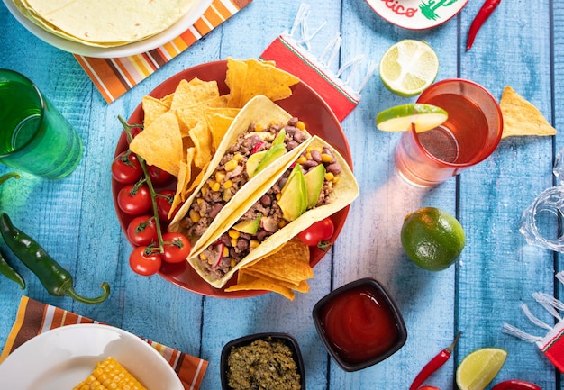 Tacos de maïs mexicains traditionnels avec de la viande, des légumes, de la salsa et des nachos aux haricots d'avocat Servis avec diverses sauces et boissons Vue de dessus Grandes réunions de famille