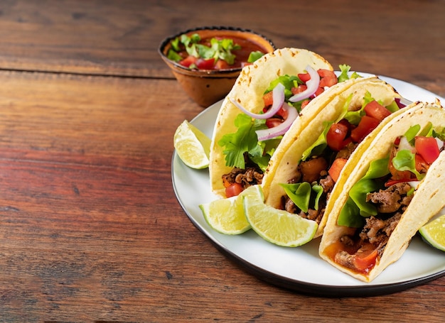 Tacos mexicains avec boeuf à la tomate et salade sur table en bois