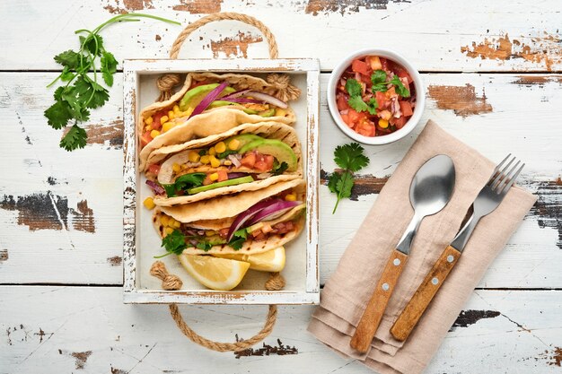 Tacos mexicains avec poulet grillé, avocat, grains de maïs, tomate, oignon, coriandre et salsa vieille table en bois blanc. Cuisine de rue traditionnelle mexicaine et latino-américaine. Vue de dessus.