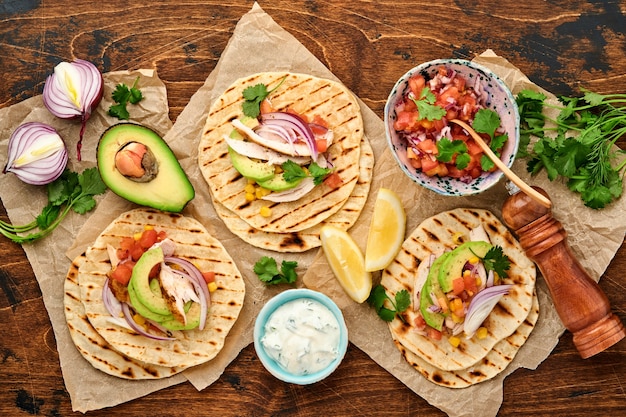 Tacos mexicains avec poulet grillé, avocat, grains de maïs, tomate, oignon, coriandre et salsa vieille table en bois. Cuisine de rue traditionnelle mexicaine et latino-américaine. Vue de dessus.