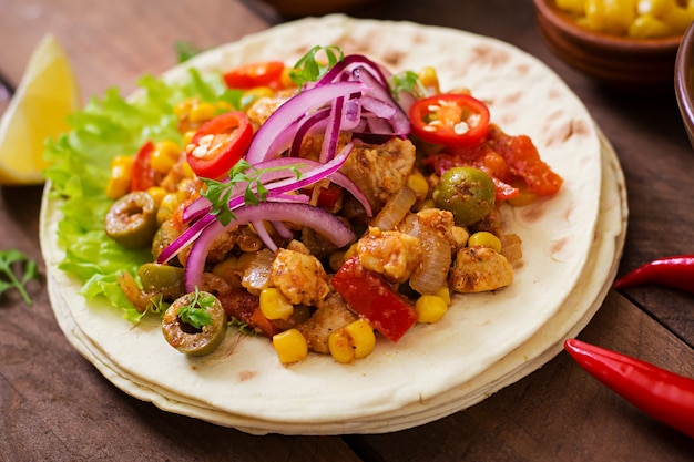 Tacos mexicains avec viande, maïs et olives sur fond en bois.