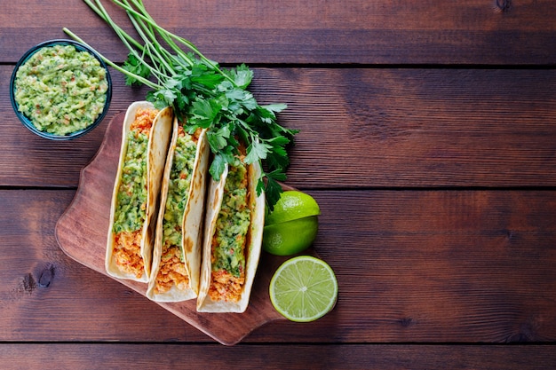 Tacos avec viande hachée frite et sauce guacamole sur une planche de bois. Tacos mexicains, coriandre et citron vert sur fond de bois. Cuisine mexicaine. Style rustique