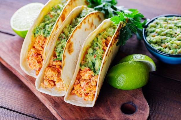 Tacos avec viande hachée frite et sauce guacamole sur une planche de bois. Tacos mexicains, coriandre et citron vert sur fond de bois. Cuisine mexicaine. Style rustique