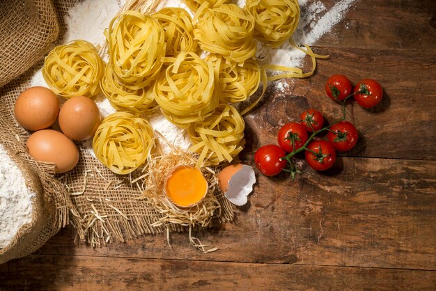 Tagliarini crus sur bois, avec tomates cerises, farine de blé et vue de dessus d'oeufs.