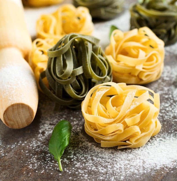 Tagliatelle Paglia e Fieno. sur fond sombre. Faire des linguines de pâtes maison sur une table de cuisine rustique avec de la farine, un rouleau à pâtisserie et des pâtes. Mise au point sélective.