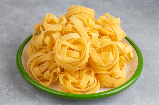 tagliatelle de pâtes à l'œuf faite maison nouilles de nid crues non cuites ruban fettuccine macaroni sec roulé long