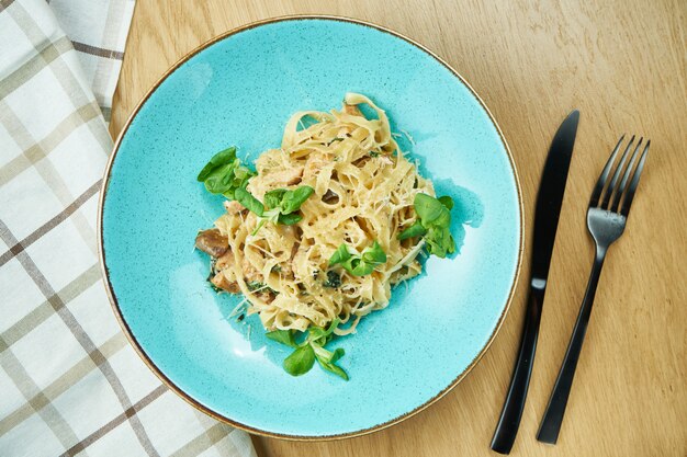 Tagliatelles au poulet, sauce blanche et parmesan dans un bol bleu sur table en bois. Pâtes italiennes traditionnelles faites maison. Fermer