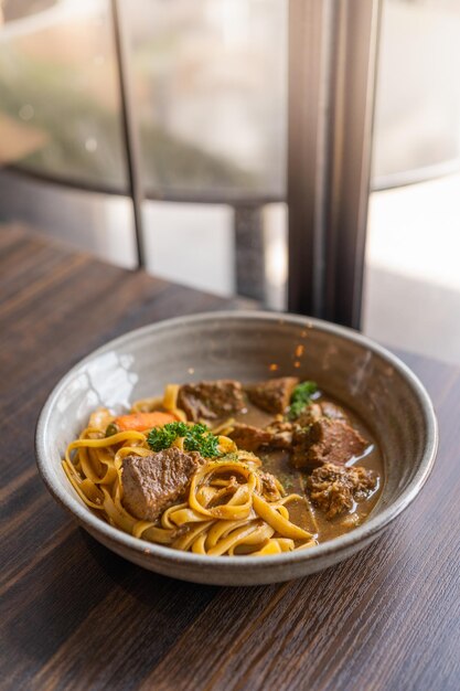 Tagliatelles au ragoût de porc et légumes dans un bol sur table en bois Spaghetti Pâtes à la viande