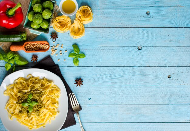 Tagliatelles de pâtes au pesto et autres légumes sur un fond de bois.