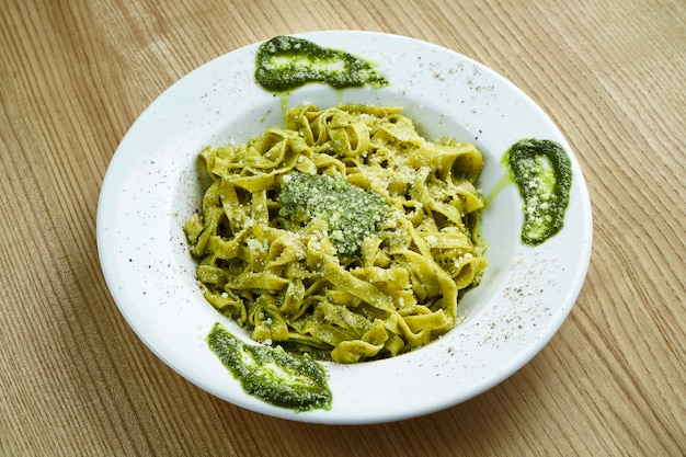 Tagliatelles de pâtes italiennes traditionnelles avec sauce au pesto et parmesan dans une assiette blanche sur une surface en bois