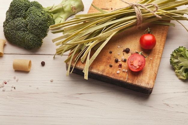 Tagliatelles vertes faites à la main avec du jus d'épinards, du brocoli, des tomates et des épices sur une table en bois blanc. Arrière-plan de cuisson des pâtes, espace de copie