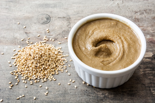 Tahini et graines de sésame sur une table en bois.