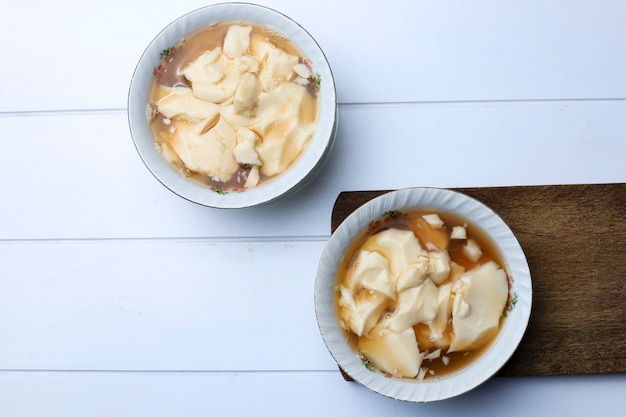 Tahwa ou Wedang Tahu ou Kembang Tahu, dessert traditionnel indonésien à base de gingembre et sirop de sucre de palme avec tofu à base de lait de soja. Servir sur un bol, vue de dessus avec espace de copie pour le texte