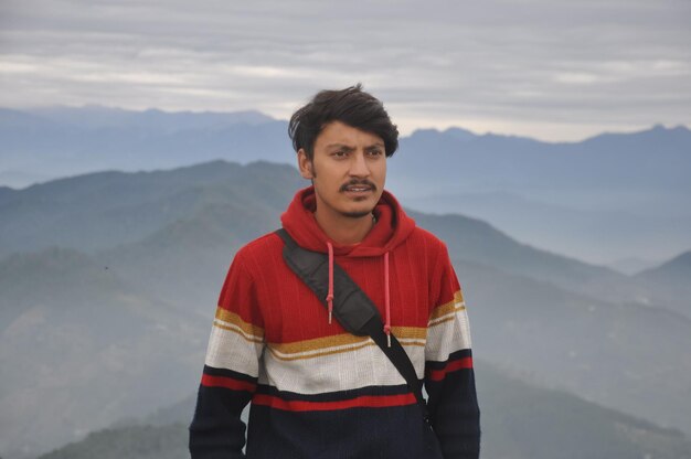 Photo taille d'un jeune homme indien regardant de côté alors qu'il se tient contre le fond des montagnes