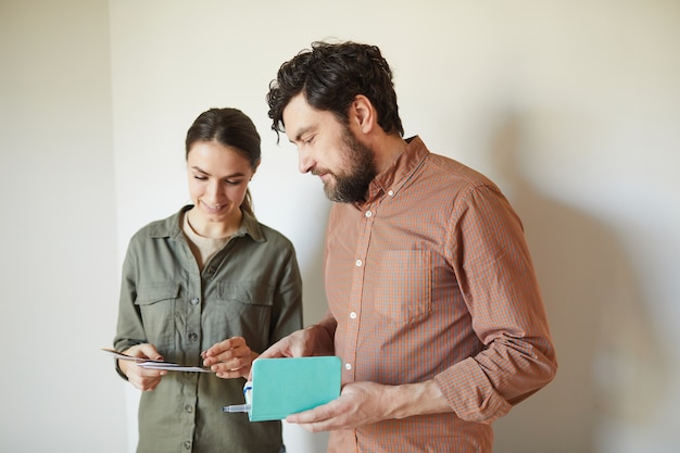 Taille portrait de couple heureux regardant des échantillons de couleur debout par mur blanc blanc tout en redécorant la maison, copiez l'espace