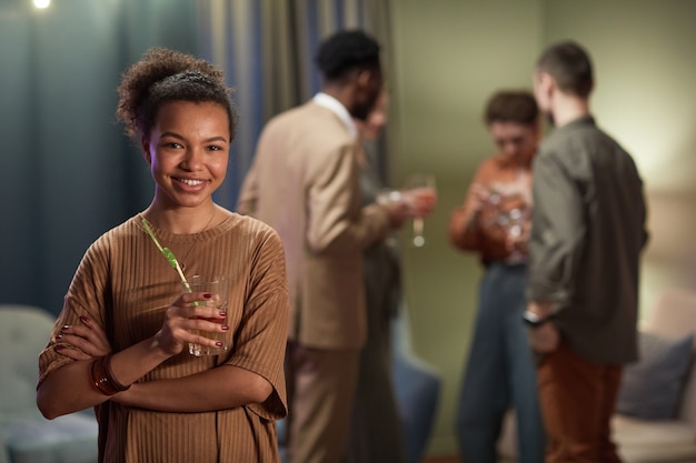Taille portrait d'une femme métisse souriante regardant la caméra et tenant un verre à cocktail tout en profitant d'une fête à la maison, espace de copie