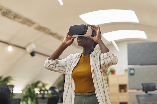 Taille portrait de jeune femme afro-américaine portant des vêtements de réalité virtuelle au bureau et profitant de la réalité immersive, copiez l'espace
