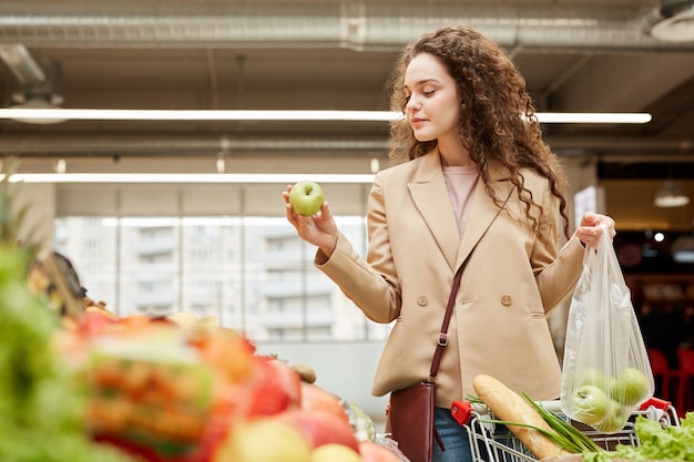 Taille Portrait De Jeune Femme Moderne Tenant La Pomme Verte Tout En Choisissant Des Fruits Et Légumes Frais Au Marché De Producteurs