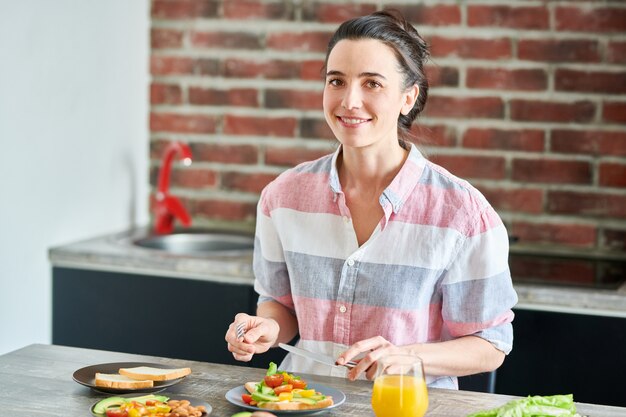 Taille portrait de jeune femme souriante en train de manger le petit déjeuner et regardant la caméra, copiez l'espace