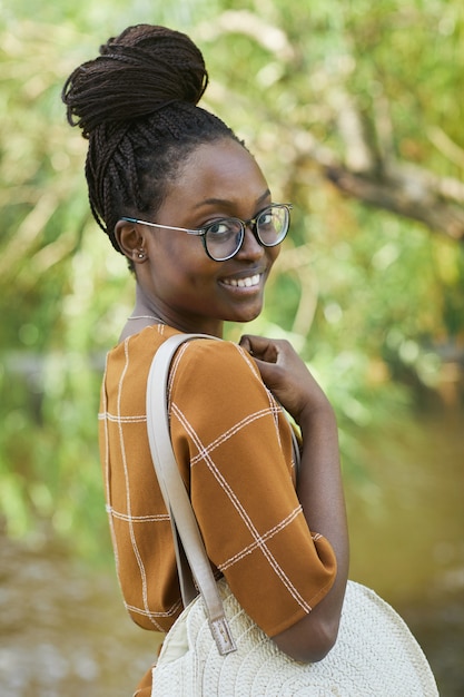 Photo taille verticale portrait de jeune femme afro-américaine portant des lunettes et souriant à la caméra dans le parc