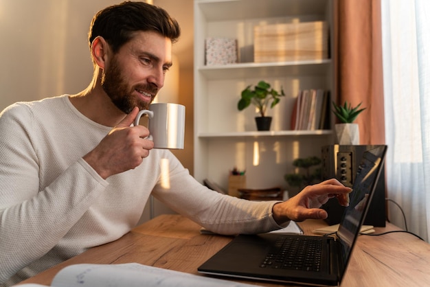 Taille vue portrait du beau jeune homme travaillant sur un ordinateur portable à la maison tout en buvant son café. Stock photo