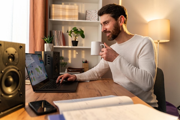 Taille vue portrait du beau jeune homme travaillant sur un ordinateur portable à la maison tout en buvant son café. Stock photo